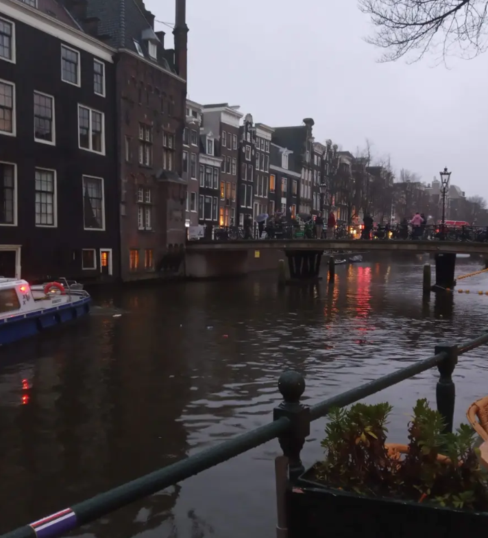 An Amsterdam canal at dusk with lit windows and a bridge